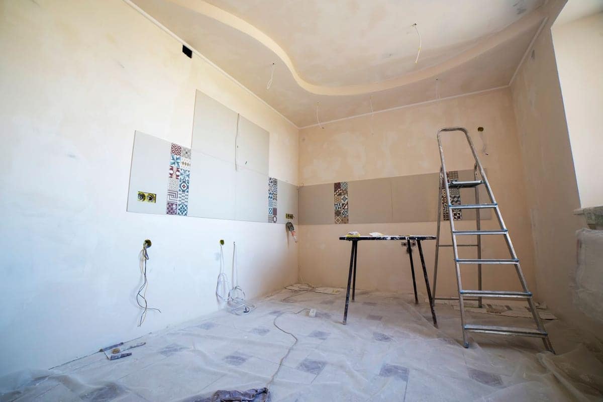 Stanza in ristrutturazione con teli di protezione, scala e punti impianto a vista